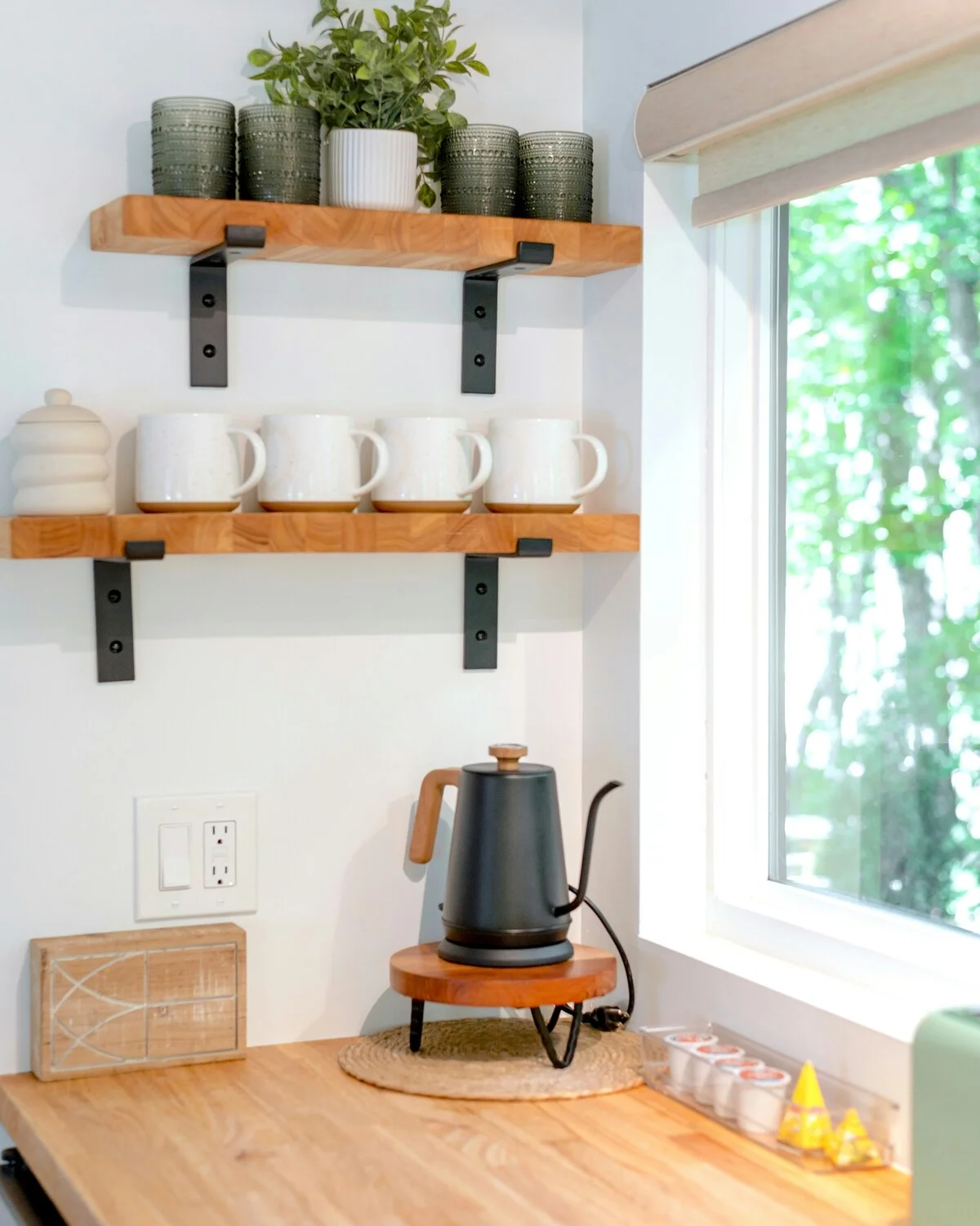Three white enamel mugs in a row on a stainless-steel bench, blurred cartons and daylight windows behind.