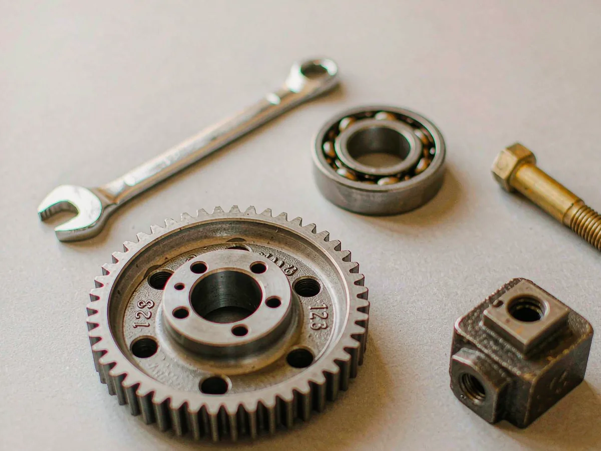 A machined gear, a ball bearing, a wrench and a brass valve arranged together on a pale surface.