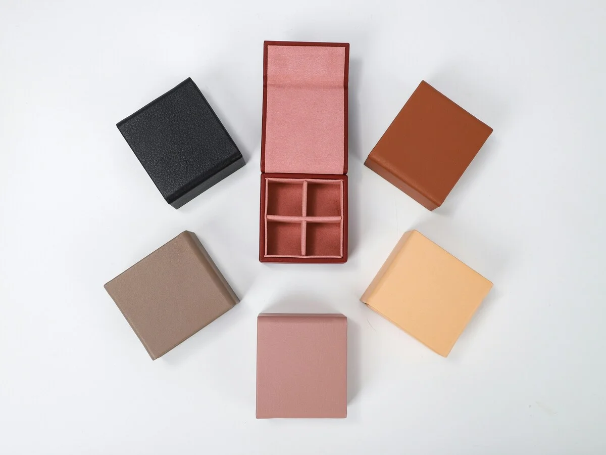 Blank paper boxes, a glass jar, a paper cup and a bubble mailer arranged together on a pale surface.