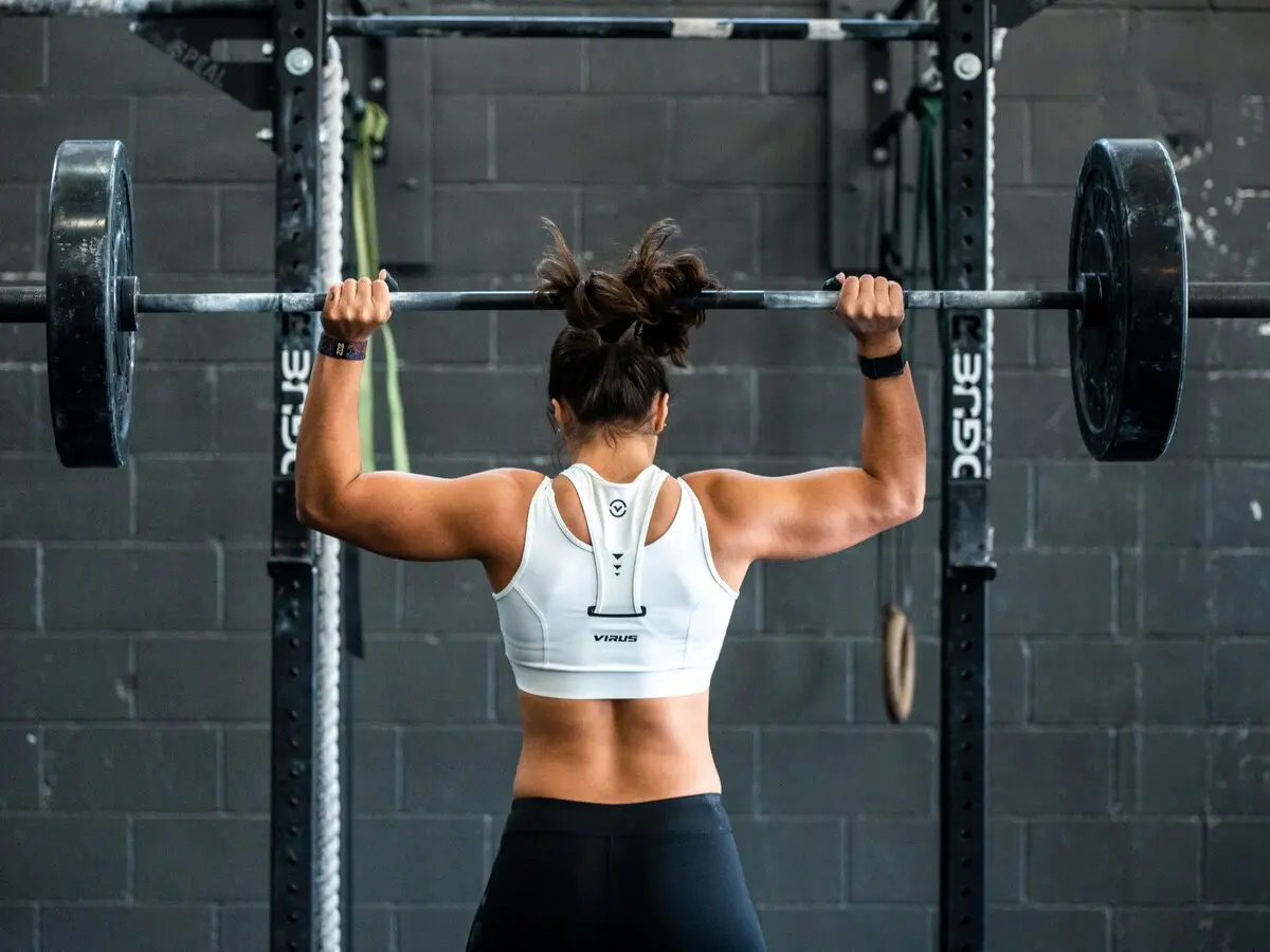 A rolled yoga mat, a dumbbell, a steel water bottle, a jump rope and a carabiner arranged together on a pale surface.